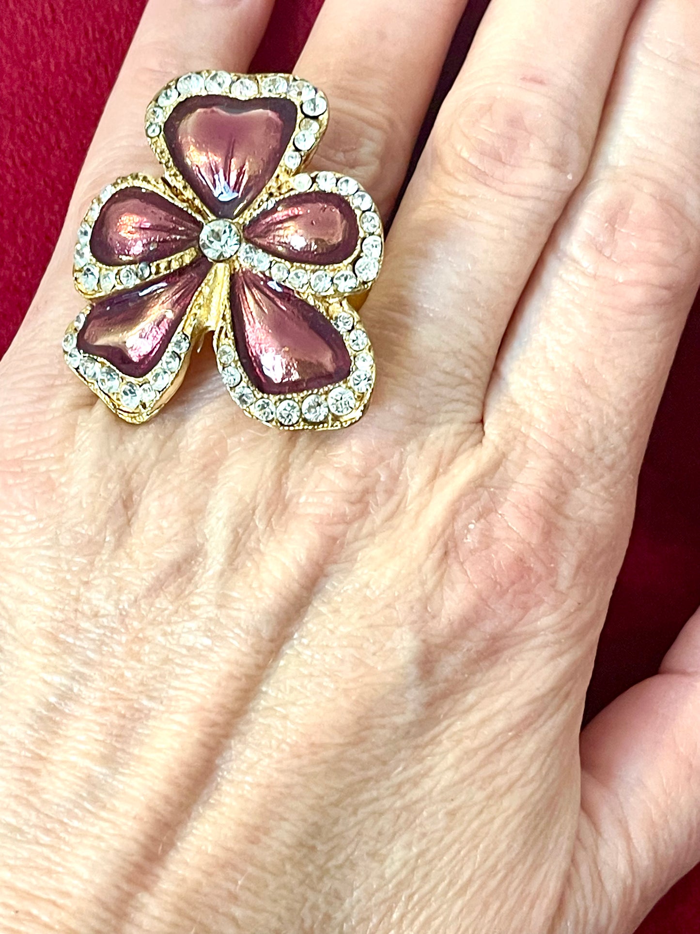 Close up Yves Saint Laurent vintage floral ring on hand, featuring metallic pink enamel petals and crystal accents in a different color shade