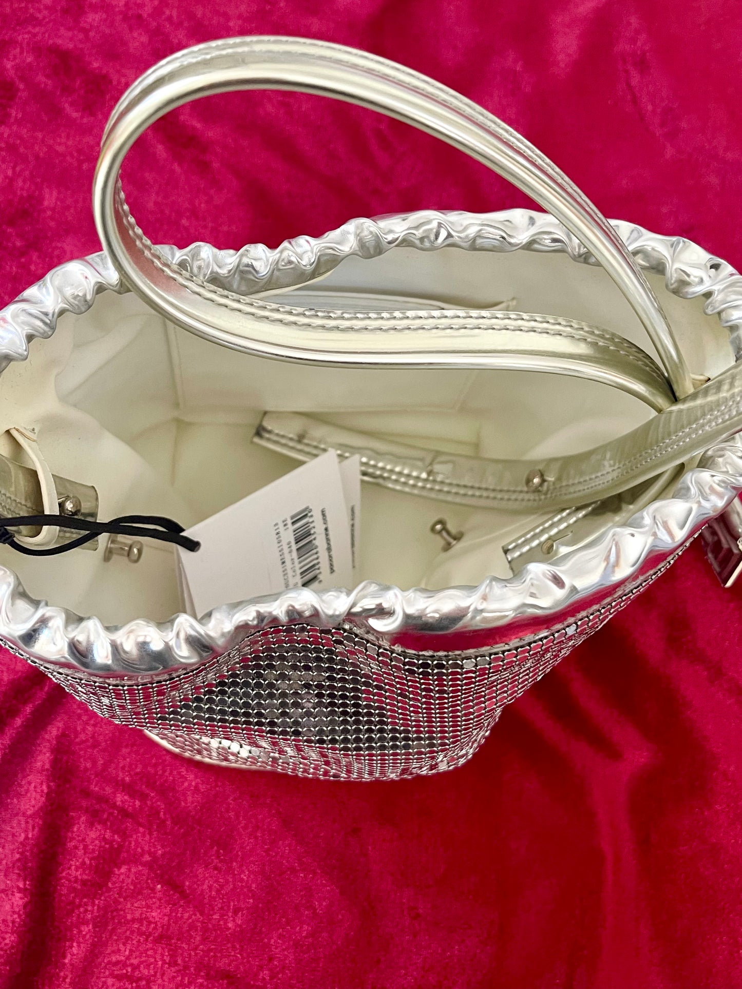 Inside view of Paco Rabanne silver shoulder/wrist bag with both straps shown, on red velvet fabric background.