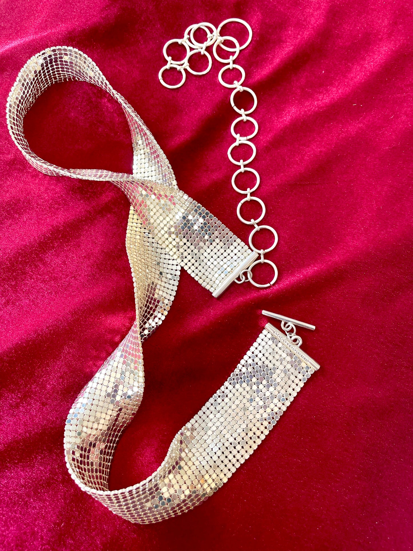 Over all view vintage silver Paco Rabanne mesh belt on red velvet background showing two sides with closure clasp and adjustable hoops