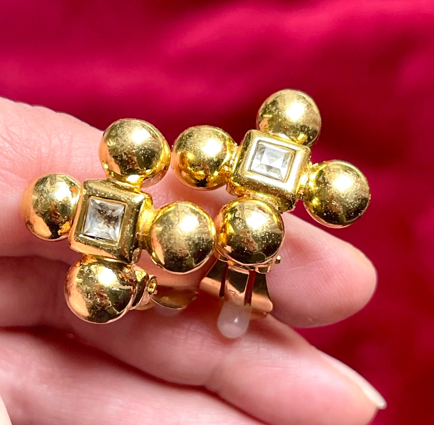 Yves Saint Laurent vintage gold tone cross clip-on earrings from the 1980s held in hand, showing rounded gold domes and square-cut center stones