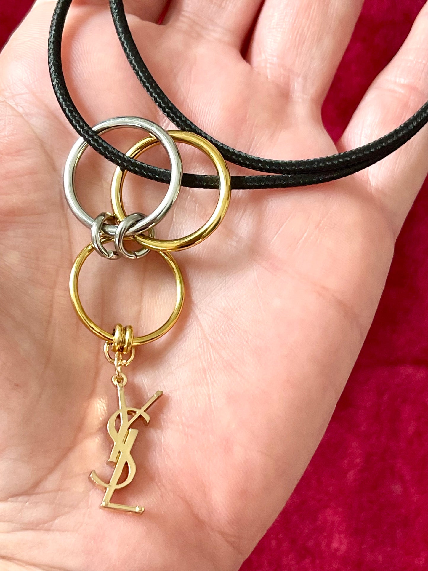 On hand close up view Yves Saint Laurent authentic charm as a ring pendant and bracelet with magnetic black cord stainless steel gold silver tone