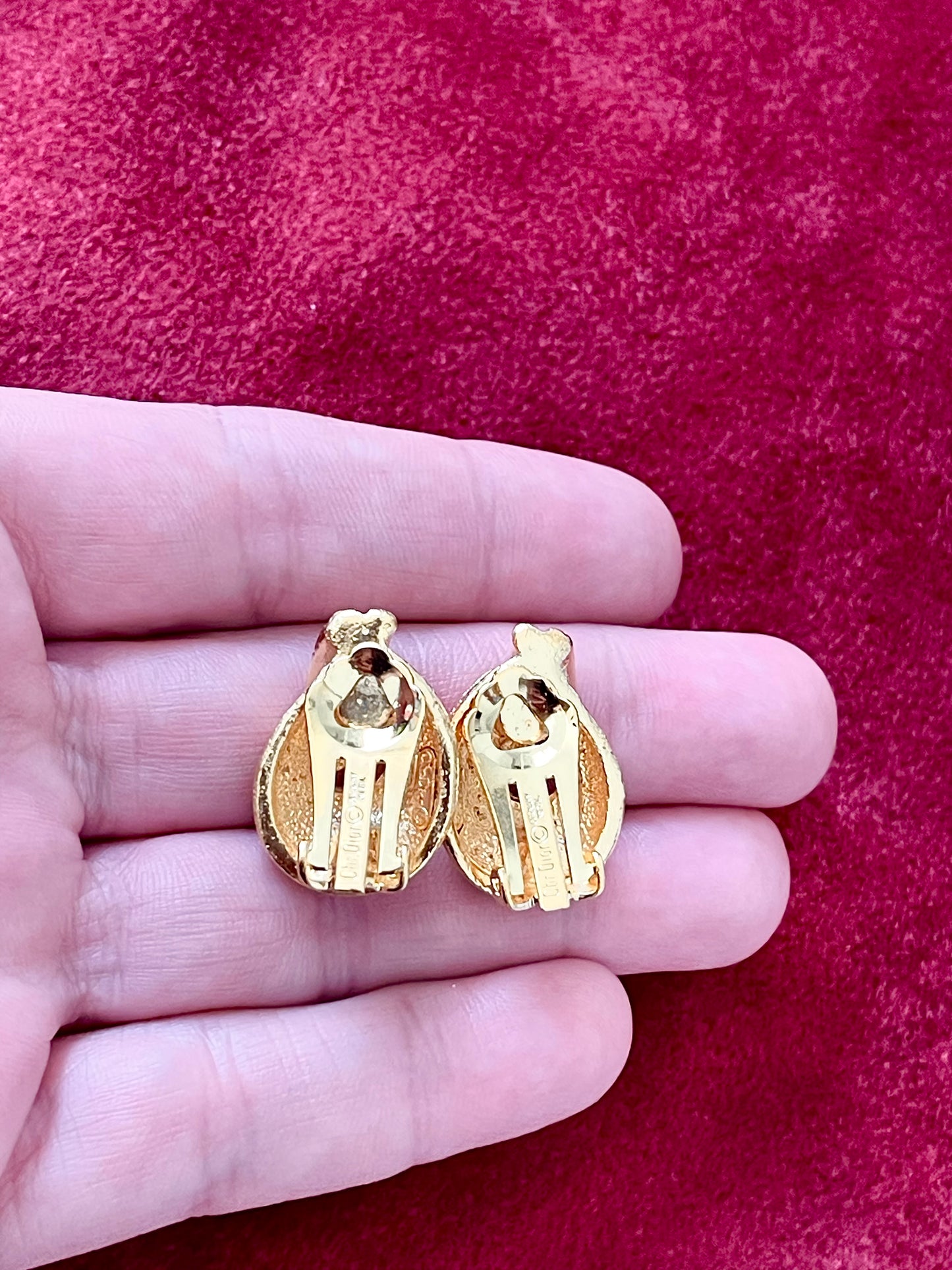 Back view on hand signature authentic Vintage Christian Dior clip on Dior earrings, gold plated 18KG displayed on a red velvet background