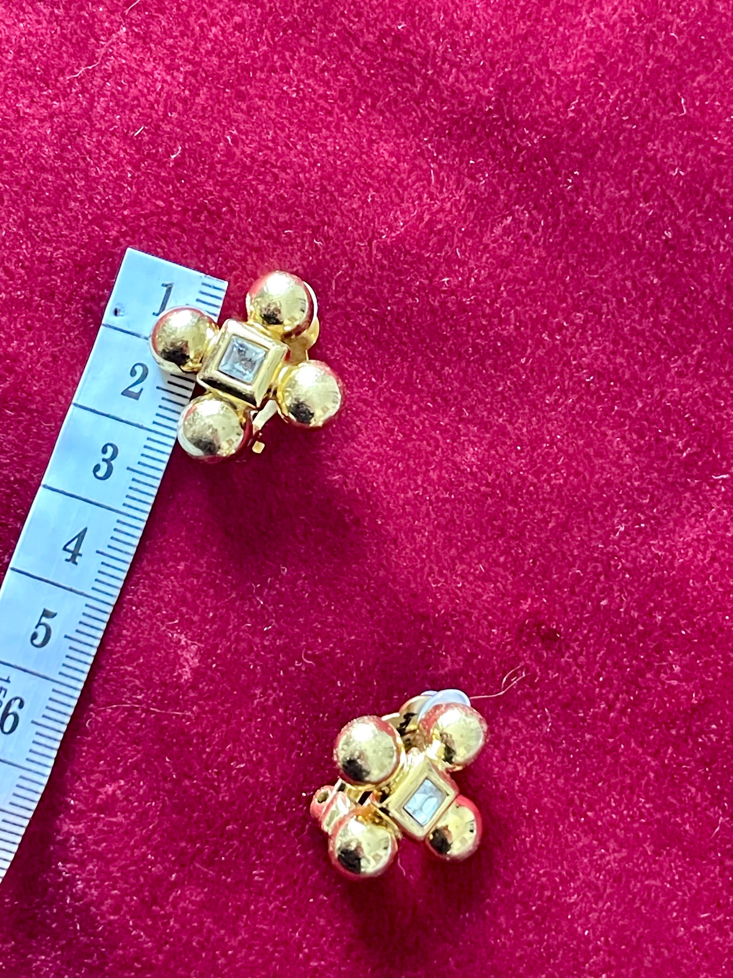 YSL vintage cross earrings displayed on red fabric background next to measuring tape, showing approximate size and subtle discoloration in one stone