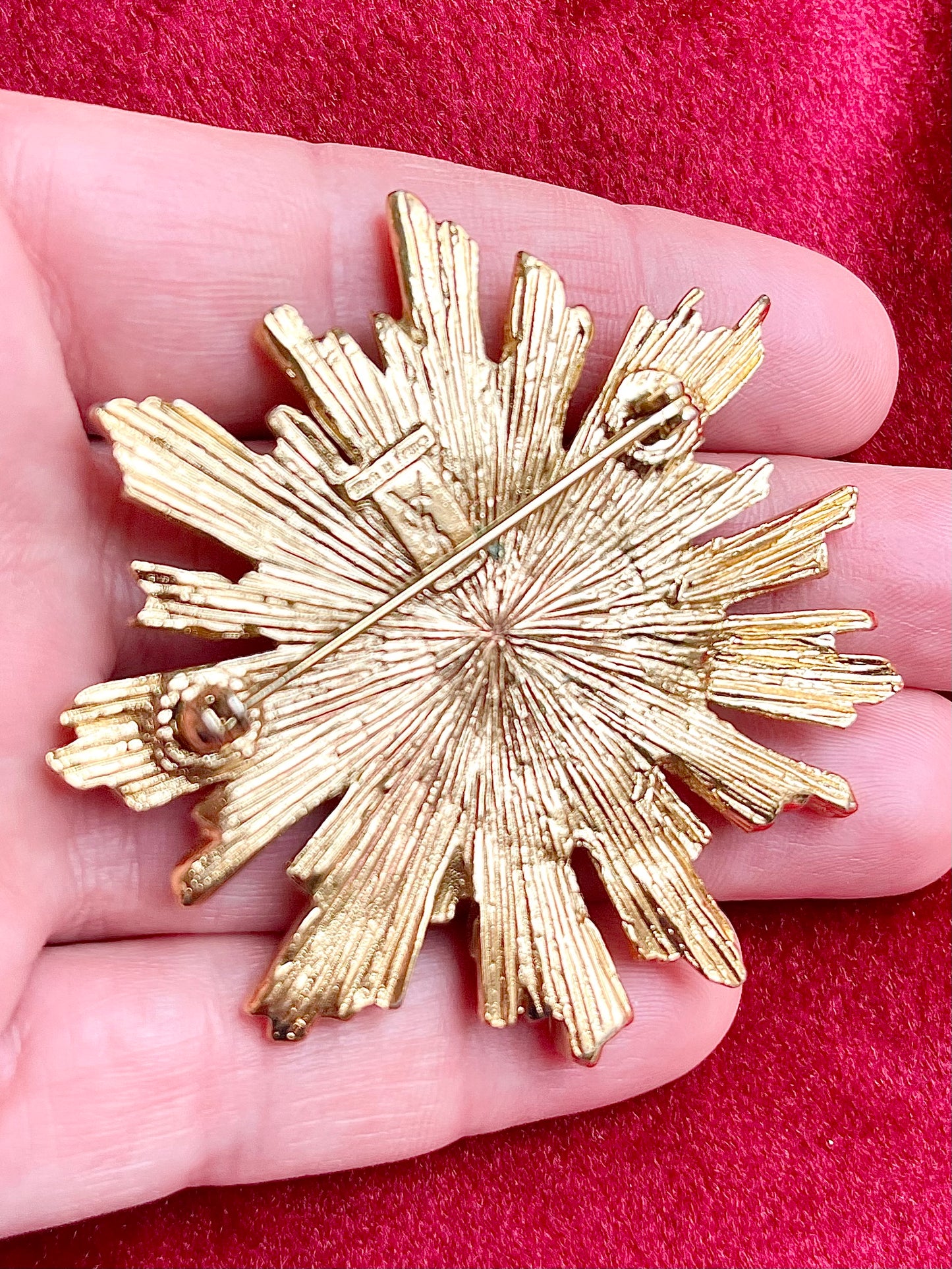 Back view signed made in France Vintage Yves Saint Laurent 1980s gold-tone sunburst brooch with green cabochon center on hand