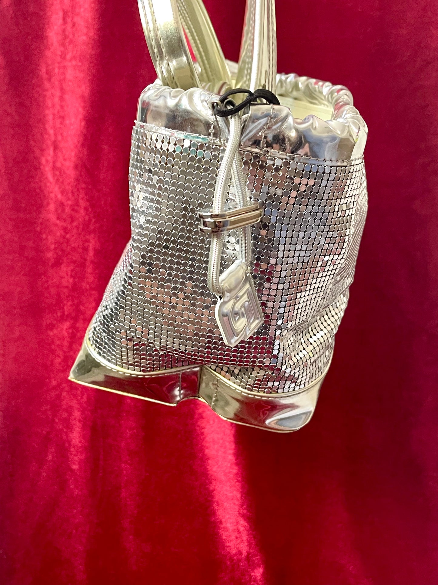 Side view of Paco Rabanne silver shoulder/wrist bag with both straps shown, on red velvet fabric background.