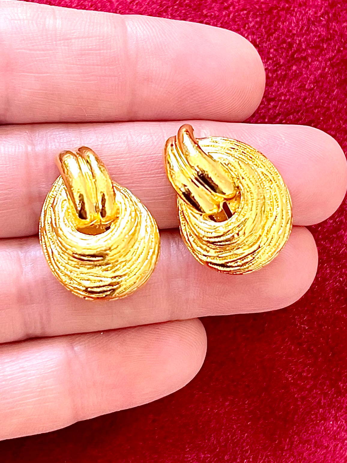 Close up on hand Vintage Christian Dior clip on Dior earrings, gold plated 18KG displayed on a red velvet background