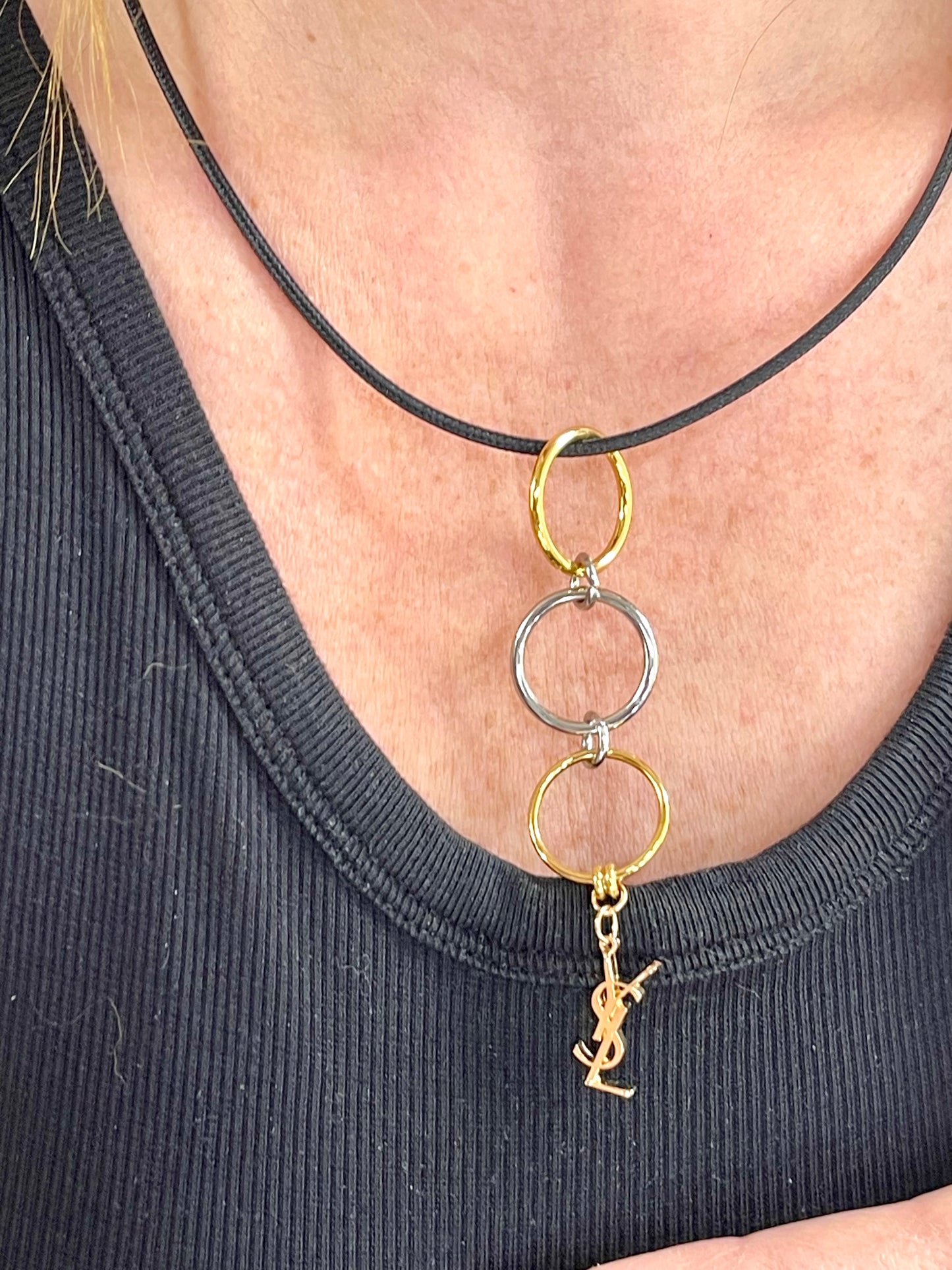 Worn by model On hand close up view Yves Saint Laurent authentic charm as a ring pendant and bracelet with magnetic black cord stainless steel gold silver tone