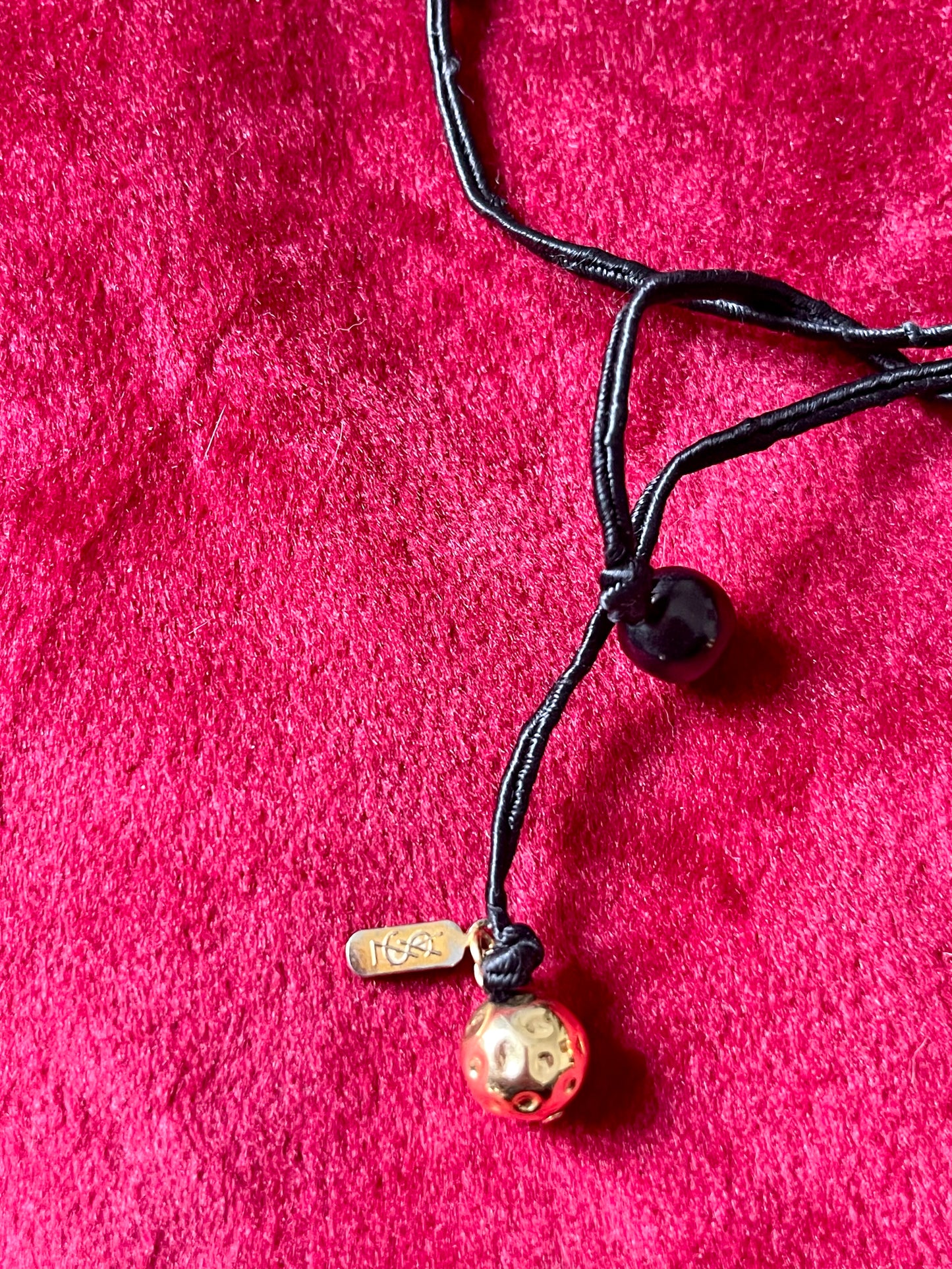 Showing authentic tag Vintage Yves Saint Laurent beaded necklace with black and gold beads, woven into braided black cotton cords, displayed on a red velvet background