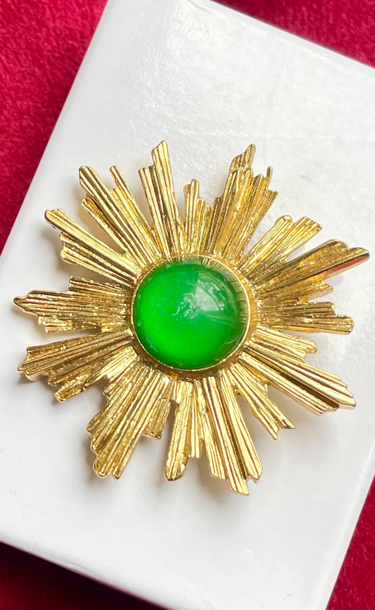 Vintage Yves Saint Laurent 1980s gold-tone sunburst brooch with green cabochon center on white display