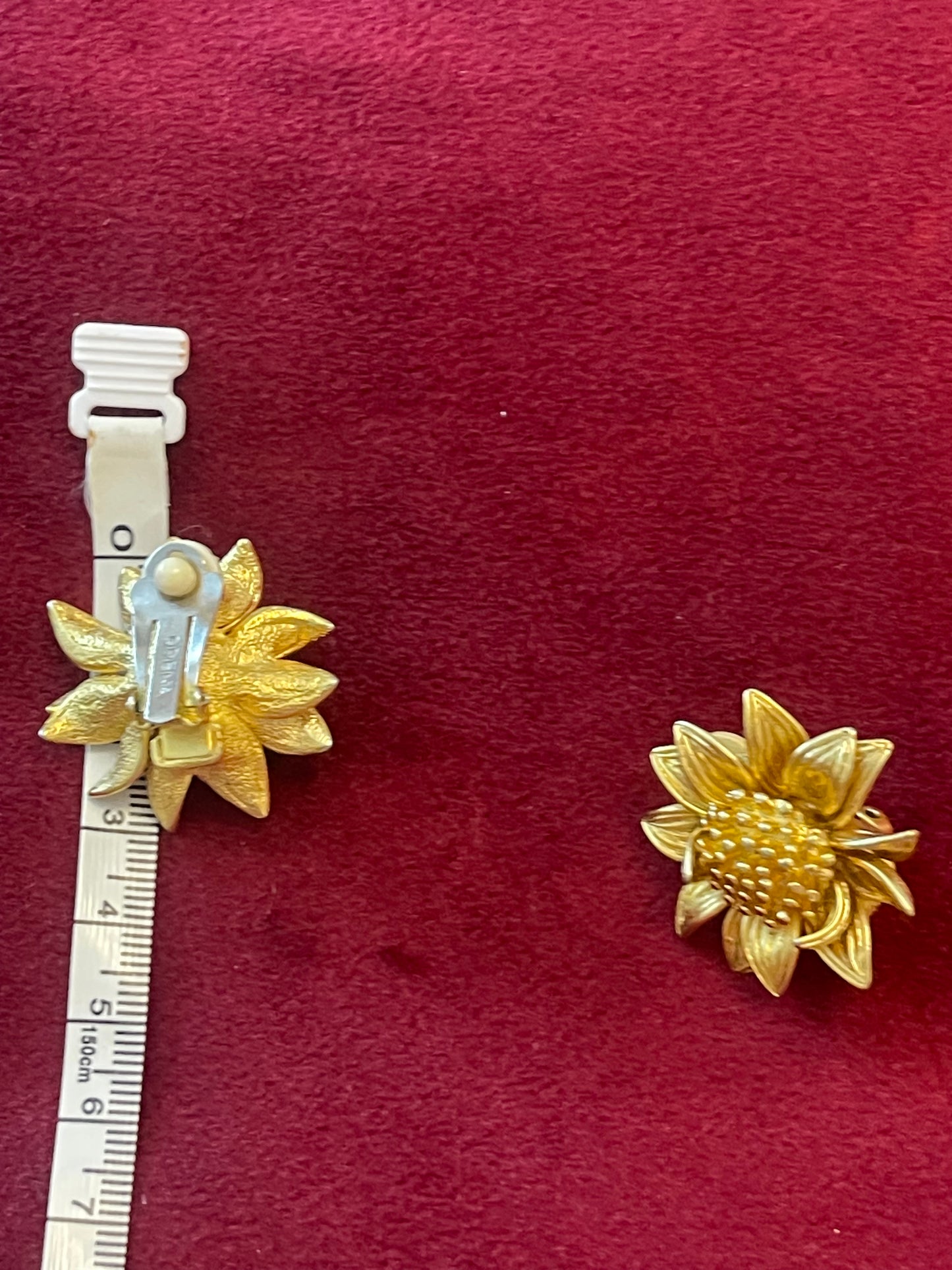 Orena Paris vintage gold sunflower-shaped earrings on a red background with a measuring tape