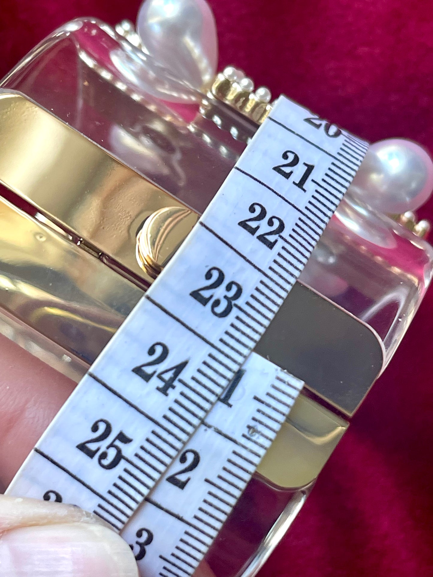 Close-up view of one transparent bracelet with a rhinestone and pearl cross design to show its gold measurement and push-button clasp mechanism. Yves Saint Laurent, Christian Lacroix, Chanel design using measuring tape