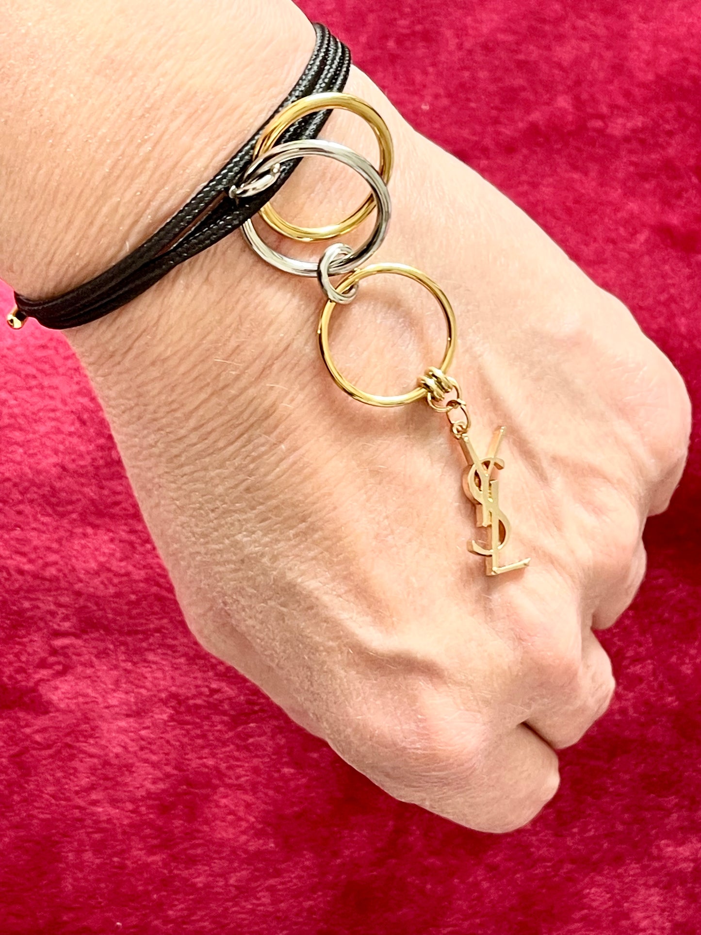 Worn as a bracelet On hand close up view Yves Saint Laurent authentic charm as a ring pendant and bracelet with magnetic black cord stainless steel gold silver tone