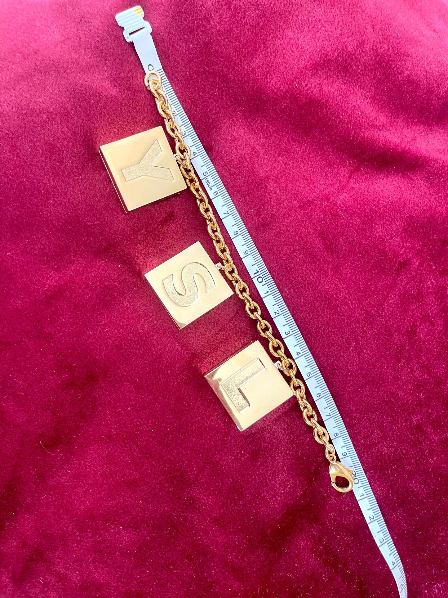 Measuring tape showing the length of YSL Yves Saint Laurent vintage 2000 makeup bracelet very good condition on red velvet background