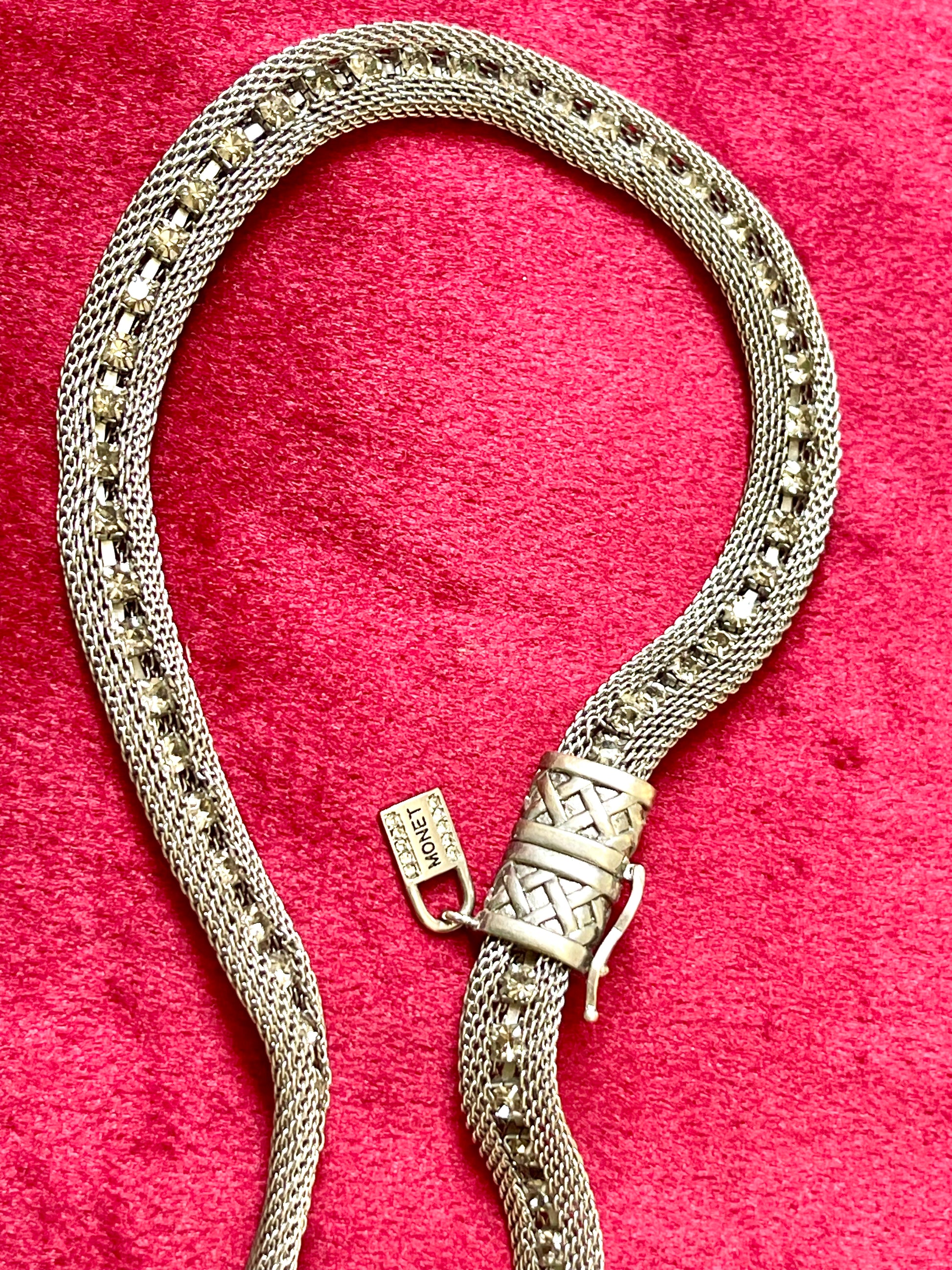 Close up Monet Yves Saint Laurent silver metal necklace rhinestone tagged chocker on red velvet background
