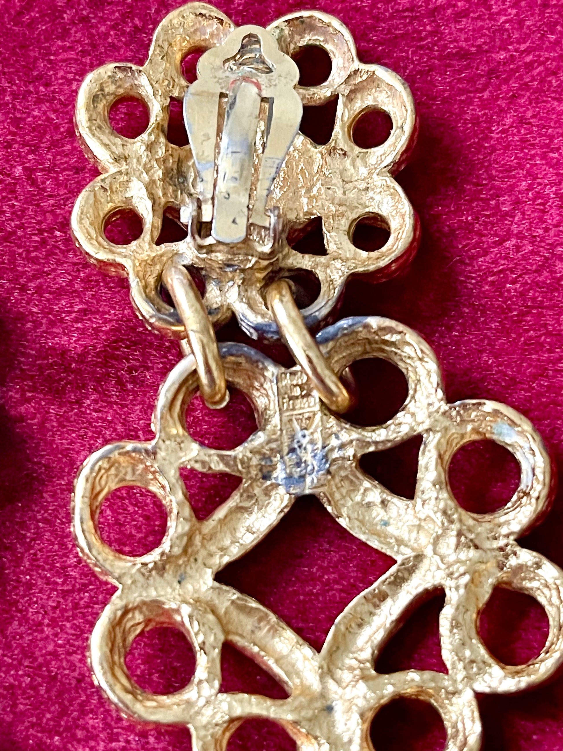 Close up on back view of vintage YSL gold-tone earrings showing textured metal, clip-on closure, and the YSL signature mark on the lower segment