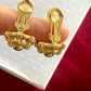 Dior Gold earrings held between fingers showing the signature against a white box background