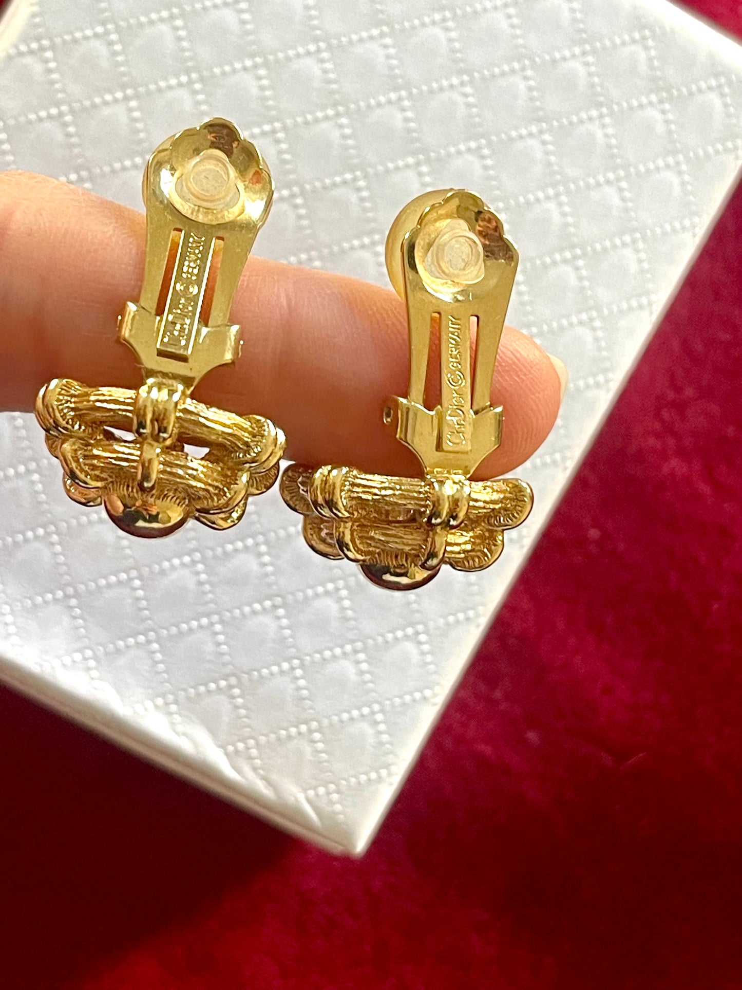 Dior Gold earrings held between fingers showing the signature against a white box background