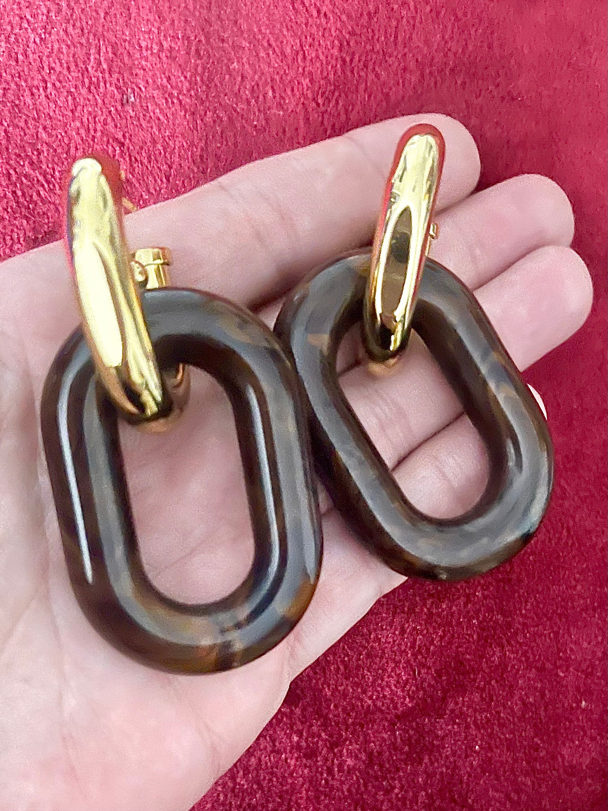 Close-up of brown resin and gold metal interlinked design of Paco Rabanne XL Link earrings, 2025 collection Held in hand 