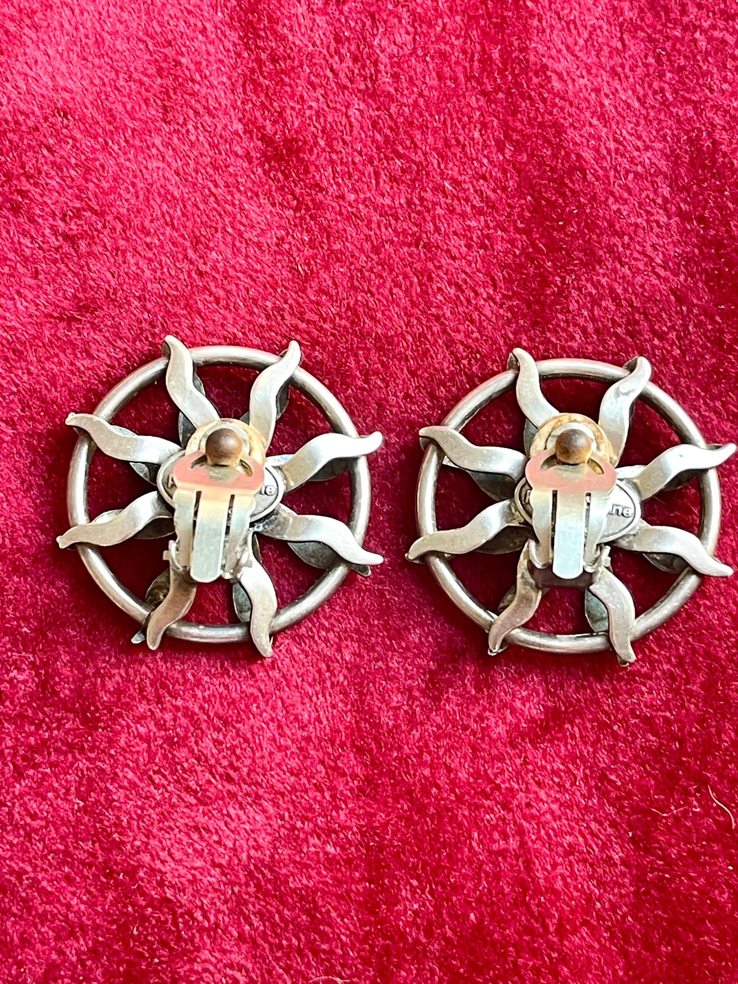 Back side view of Vintage Paco Rabanne sun-design earrings in silver tone with black faceted stones, shown against a red fabric background.
