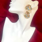 Pair of gold-tone vintage Yves Saint Laurent heart-shaped clip-on earrings decorated with multi-colored crystals, displayed on a mannequin bust on a red background