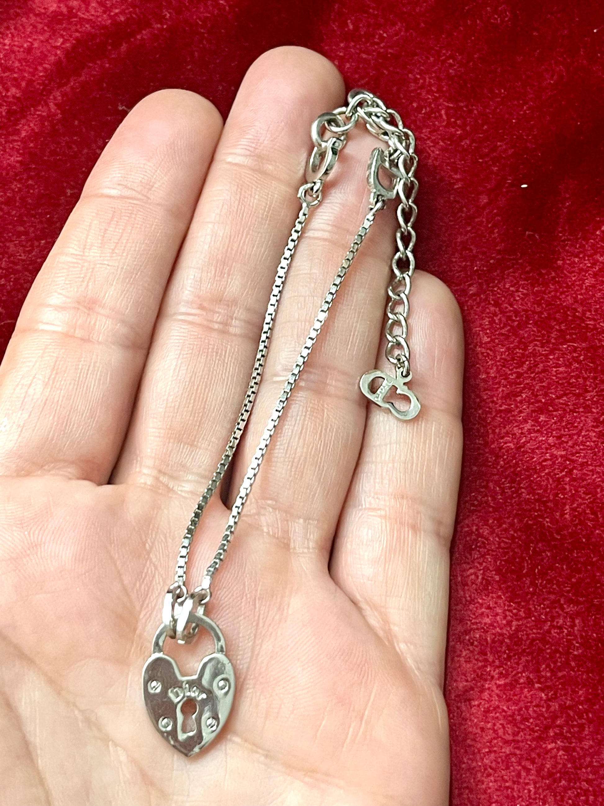 Silver Dior bracelet with a heart-shaped pendant held in a hand against a red background