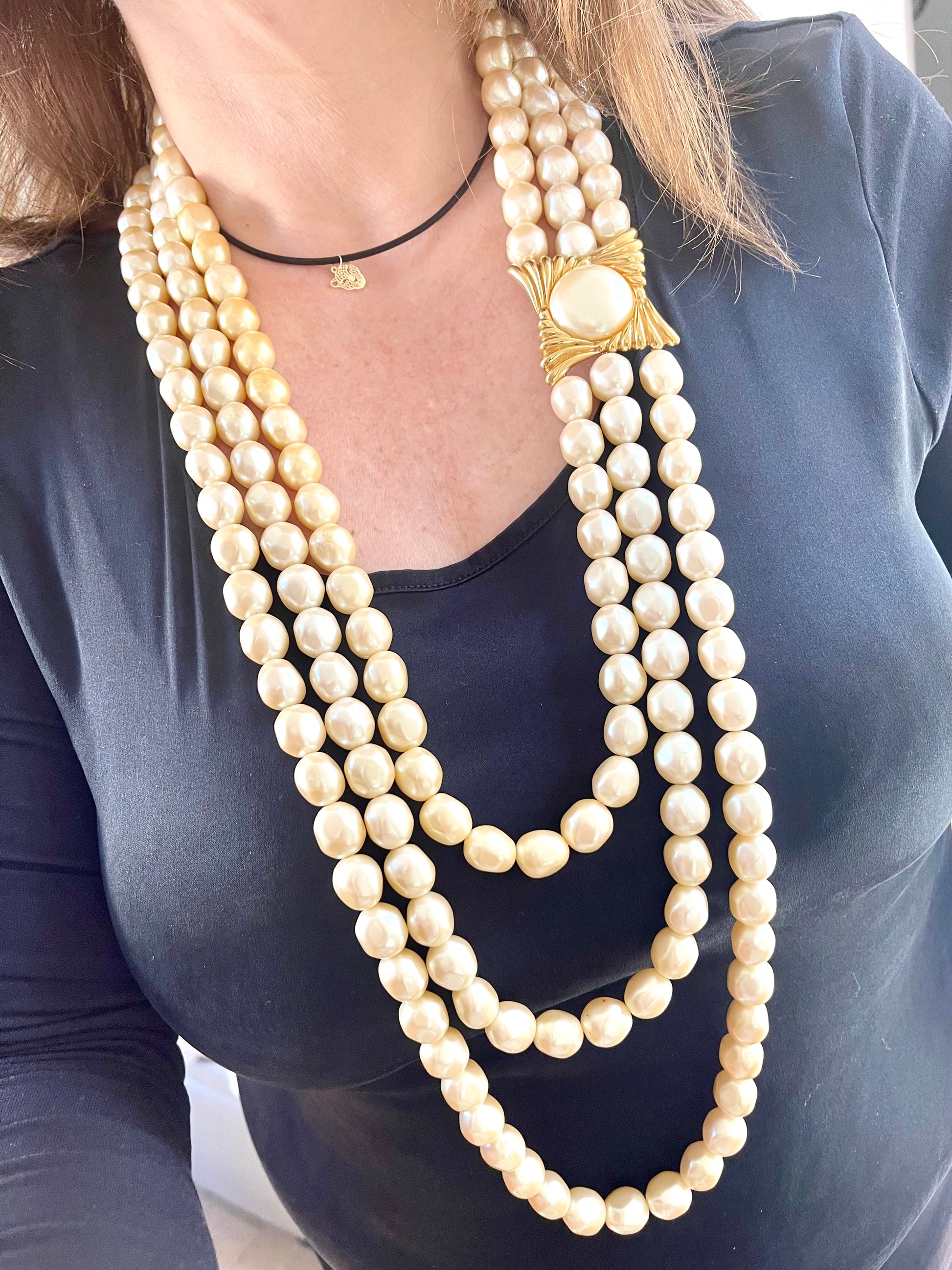 Close-up of YSL faux pearl necklace clasp worn on neck, highlighting the gold-tone sculptural design and domed pearl centerpiece