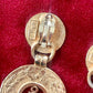 Close up on Back of Yves Saint Laurent gold-tone anchor earrings with engraved signatures red background 