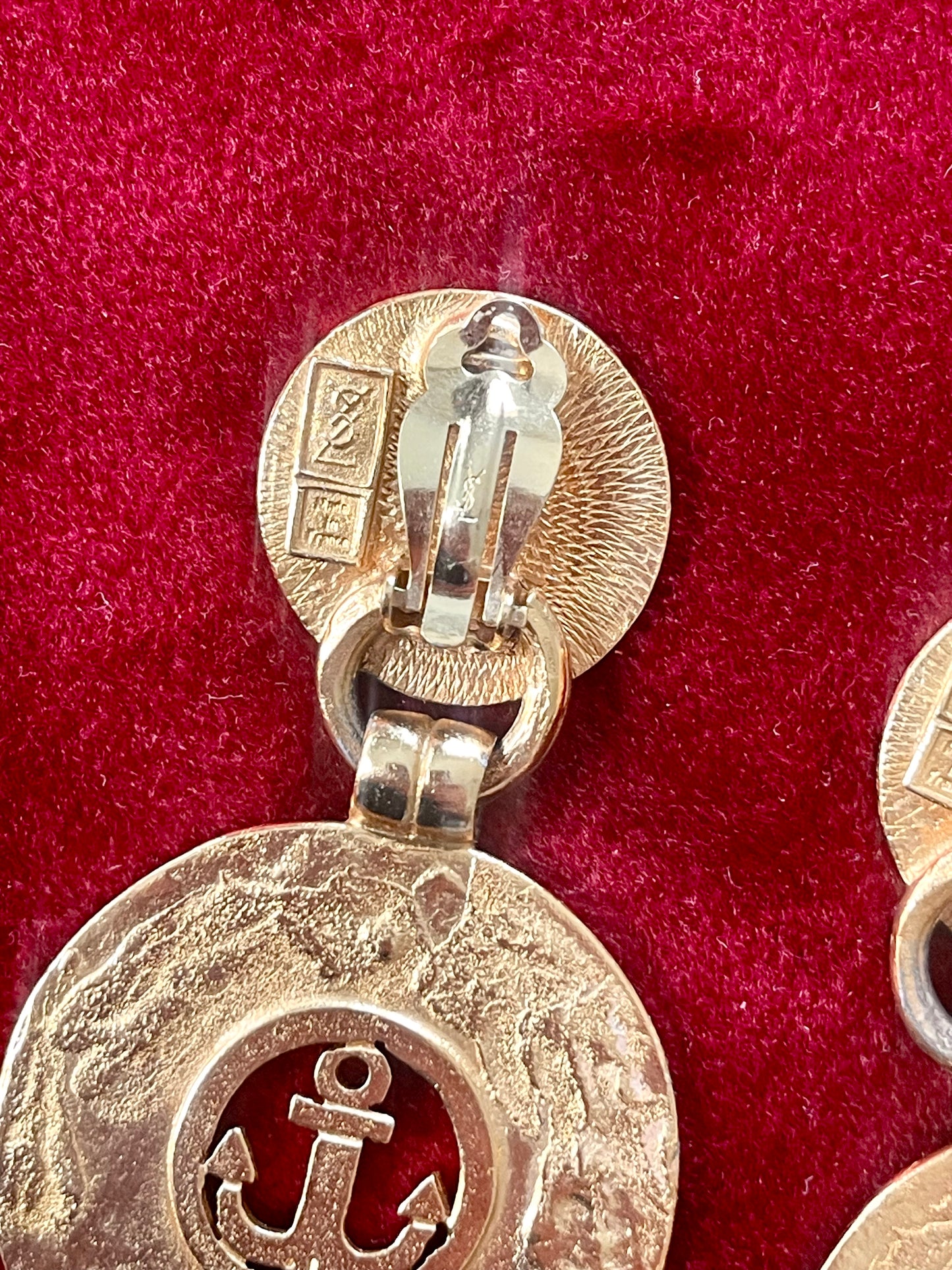 Close up on Back of Yves Saint Laurent gold-tone anchor earrings with engraved signatures red background 