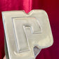 Bottom view of Paco Rabanne silver shoulder/wrist bag with both straps shown, on red velvet fabric background.