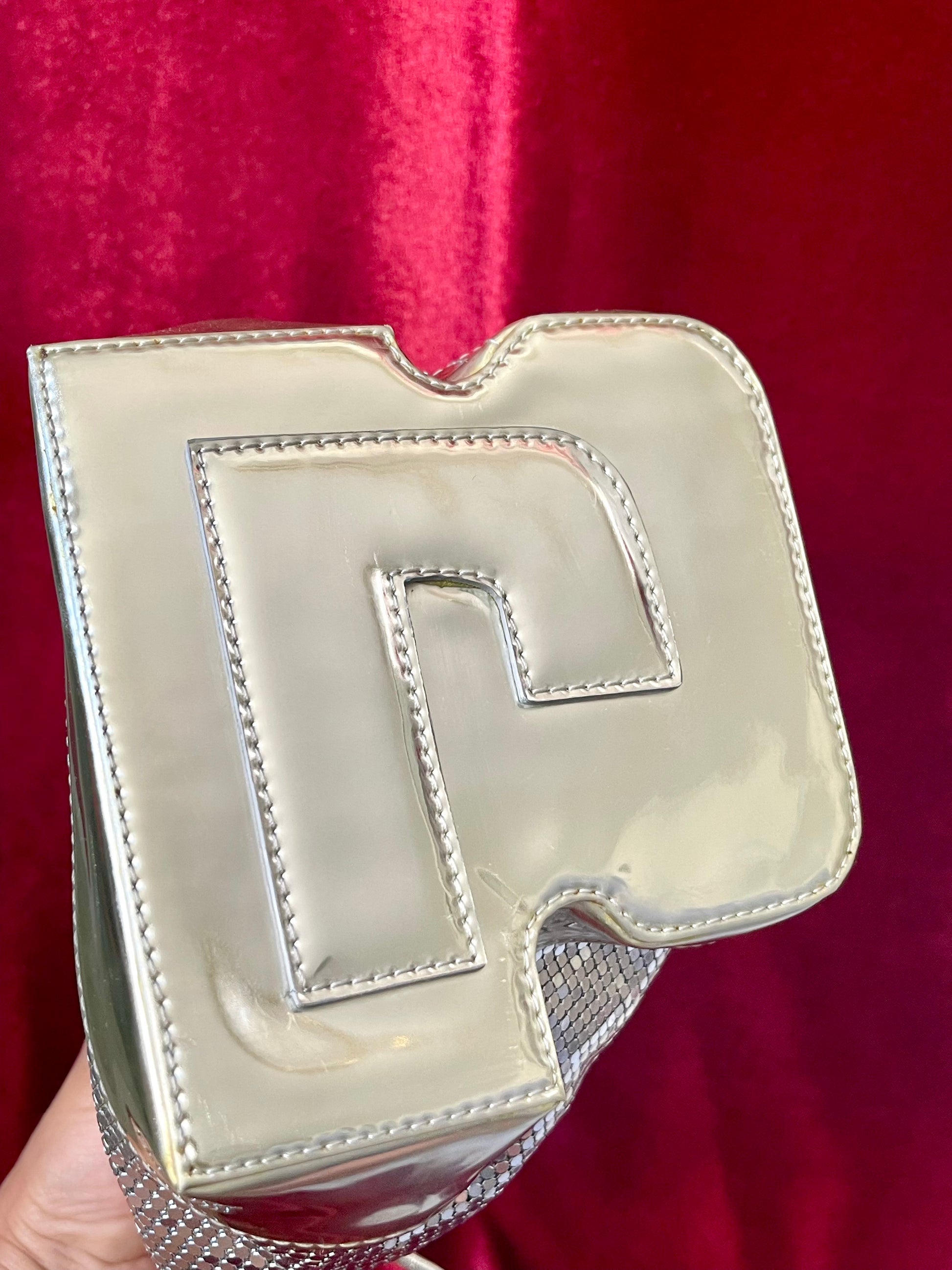 Bottom view of Paco Rabanne silver shoulder/wrist bag with both straps shown, on red velvet fabric background.
