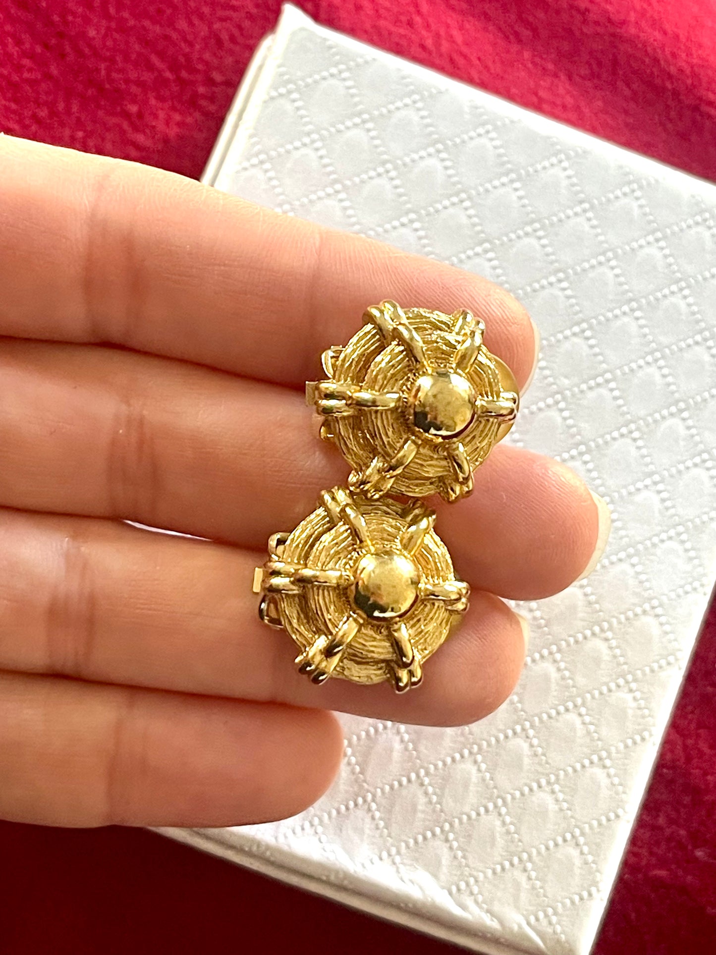 Close up view of vintage Christian Dior button earrings, held by hand against a pink background 