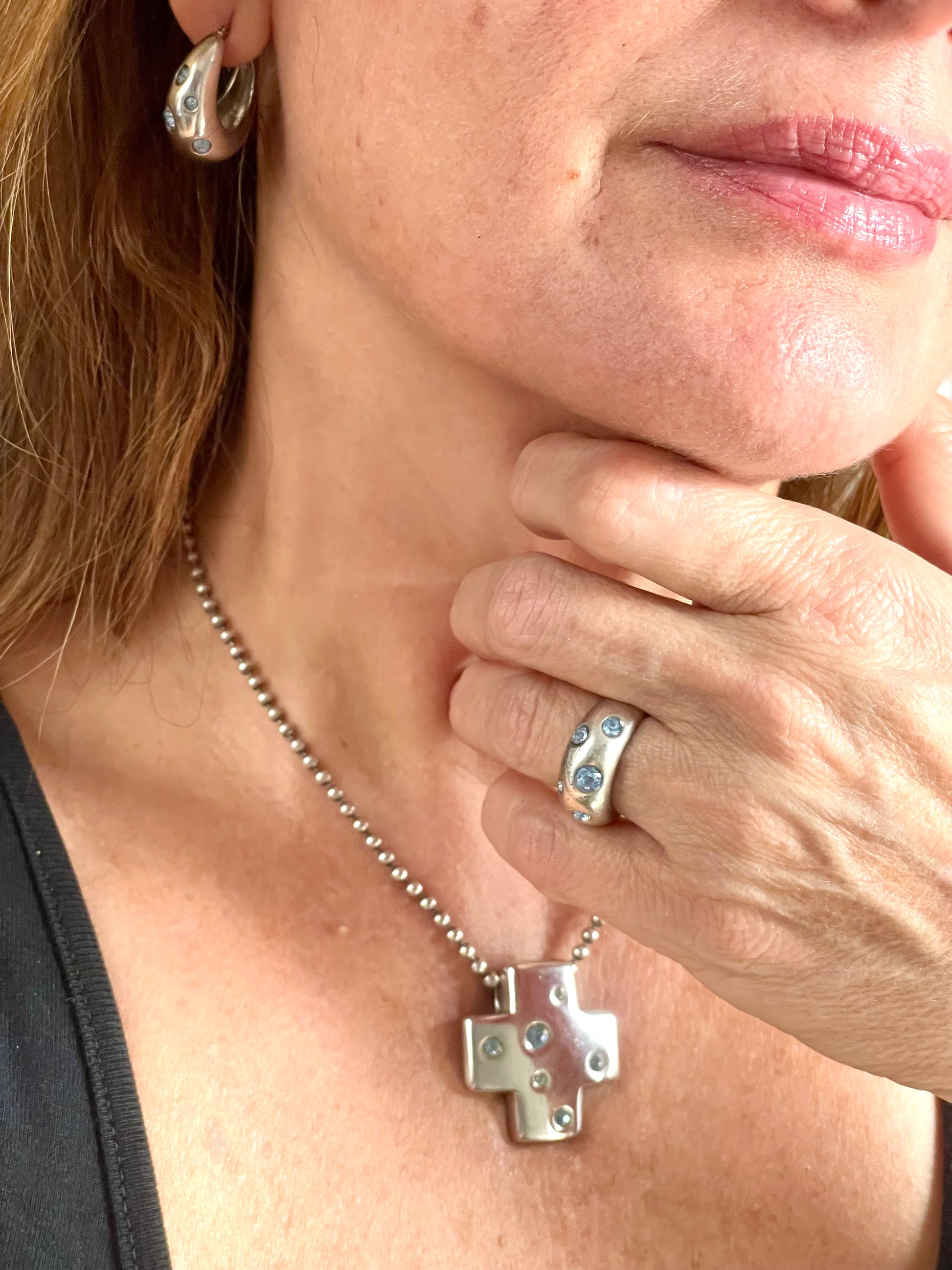 Close-up of a person wearing the vintage YSL jewelry set: silver earrings with blue stones, cross pendant necklace, and matching ring