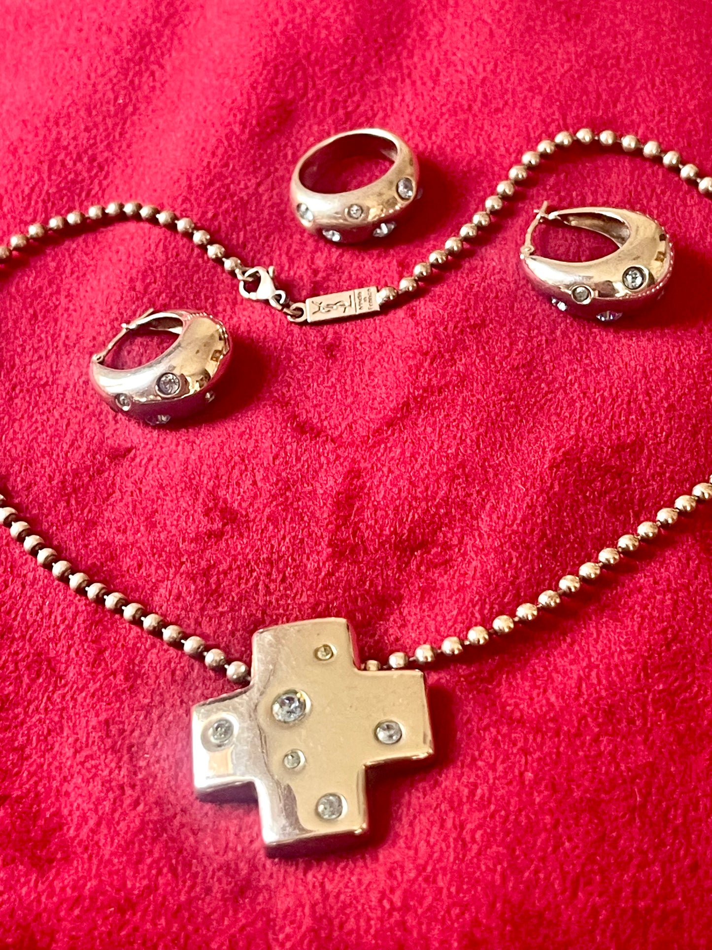 Vintage YSL silver jewelry set displayed on red fabric: silver earrings, cross pendant necklace on beaded chain and ring 