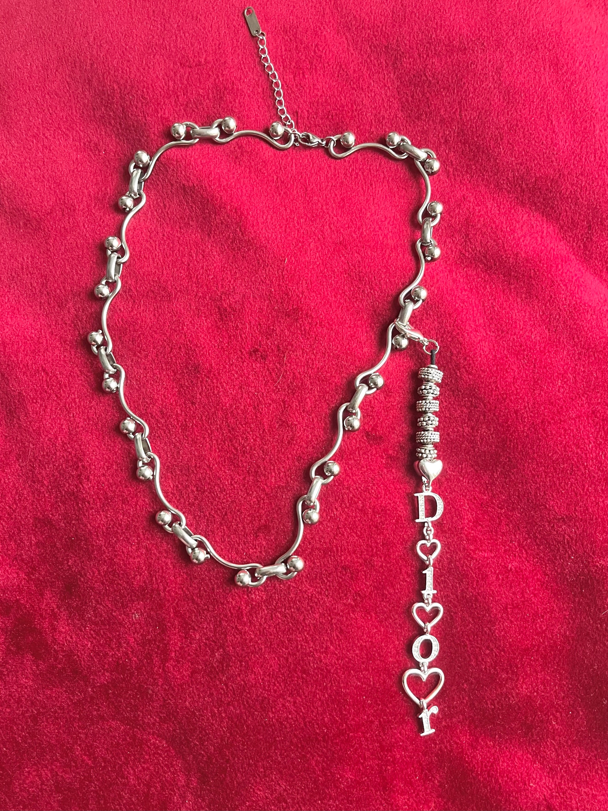Upcycled Dior pendant necklace displayed fully extended, adjustable silver-tone stainless steel chain On red background 