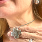 Close-up of a person wearing the vintage YSL jewelry set: silver earrings with blue stones, cross pendant necklace, and matching ring
