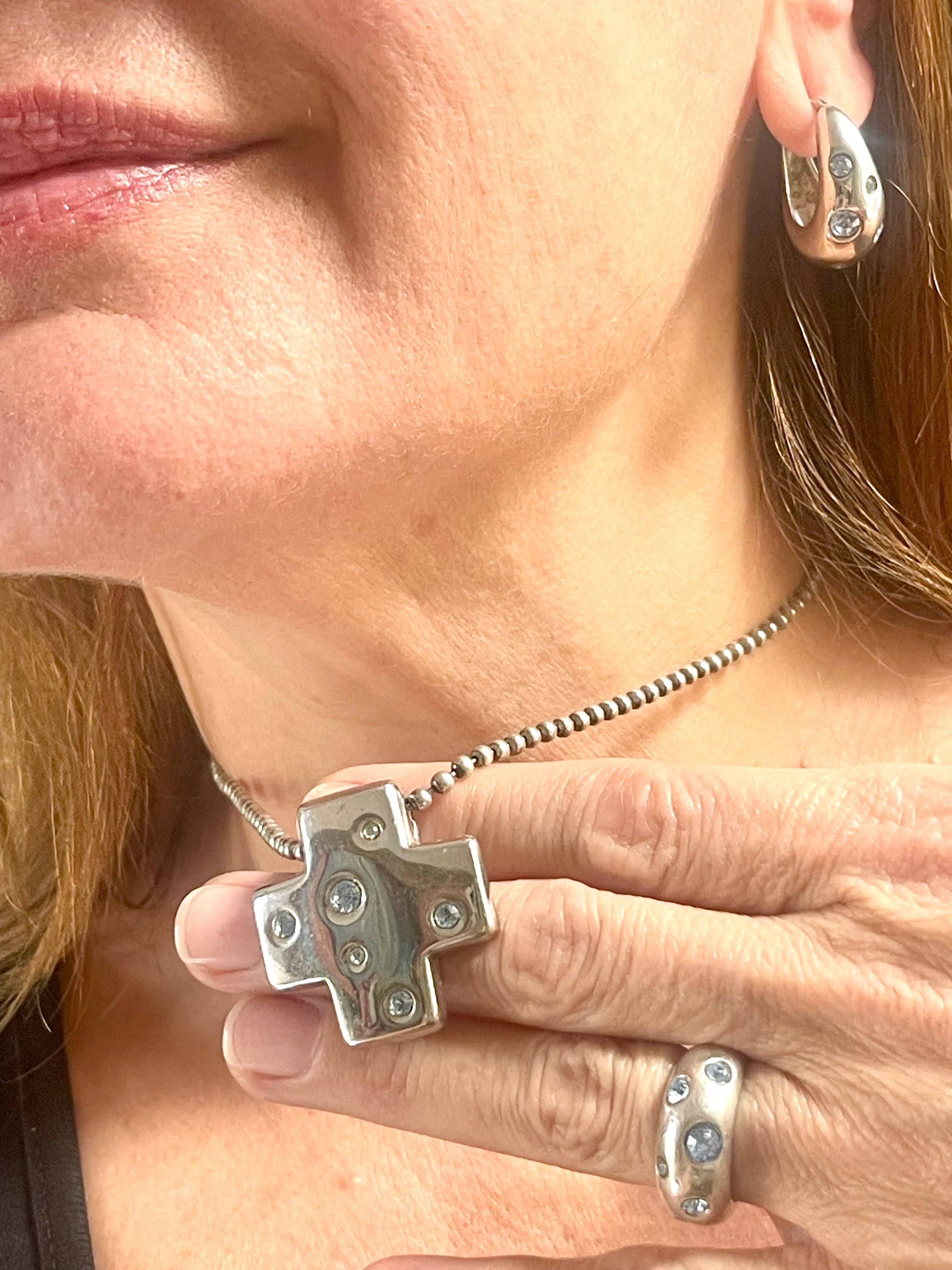 Close-up of a person wearing the vintage YSL jewelry set: silver earrings with blue stones, cross pendant necklace, and matching ring