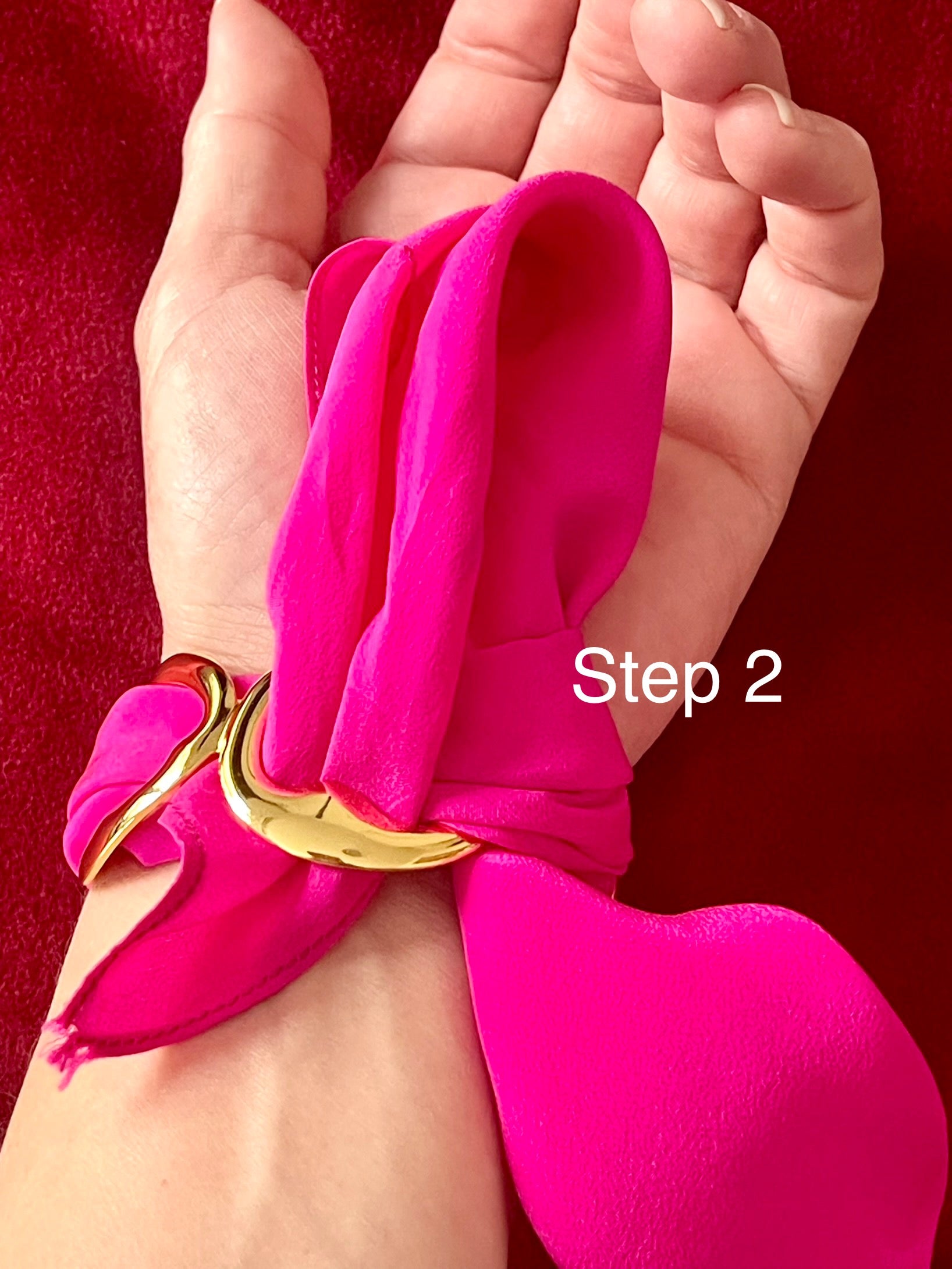 Hand wearing a bright Dior pink scarf bracelet with a gold tone on a red background, labeled 'Step 2'.