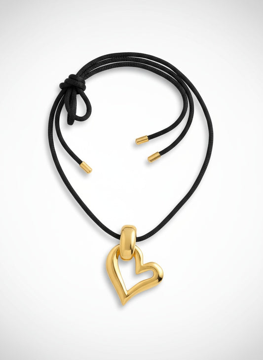 Gold heart-shaped pendant yves saint laurent on a black cord against a white background