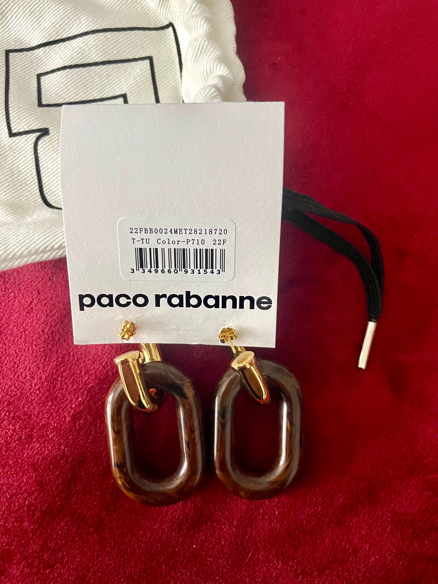 Paco Rabanne XL Link earrings on a red surface with a white card displaying the brand name.