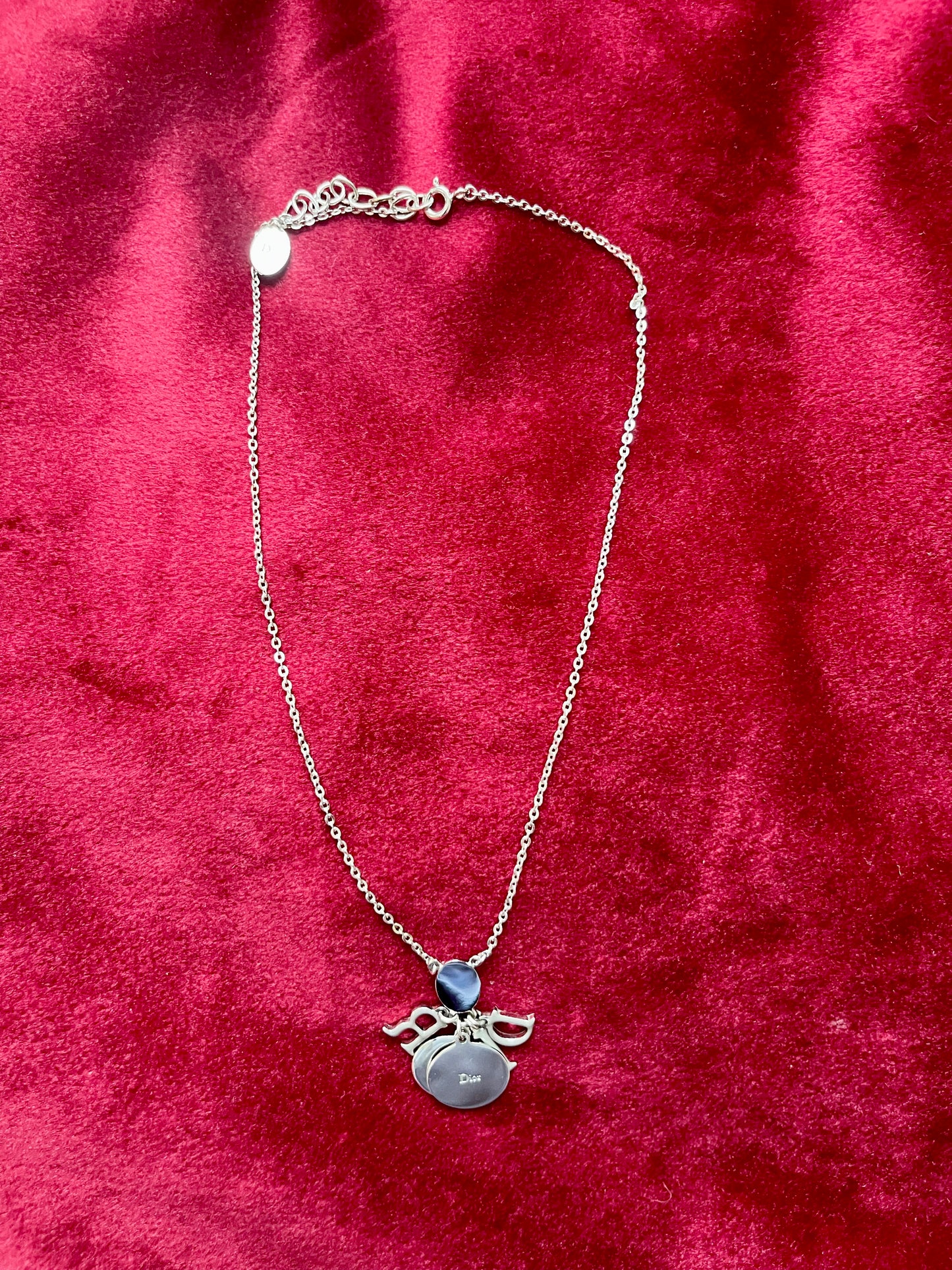 Backside view of the Dior necklace showing the reverse of the letter charms and chain on red velvet fabric.
