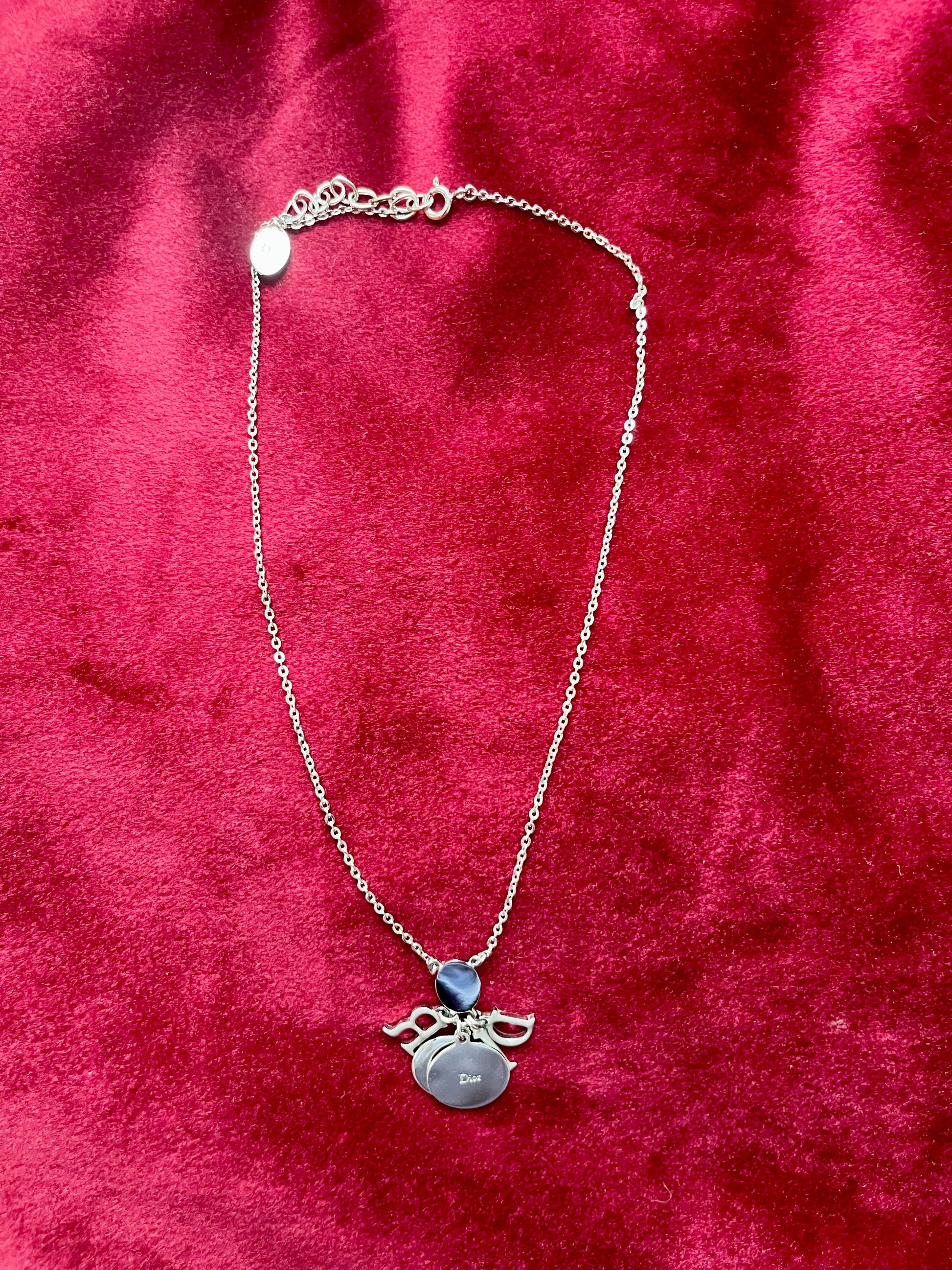 Backside view of the Dior necklace showing the reverse of the letter charms and chain on red velvet fabric.