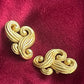 Vintage Nina Ricci swirly heart earrings in matte gold plated metal, signed Nina Ricci Paris, 1990s design on a red background 