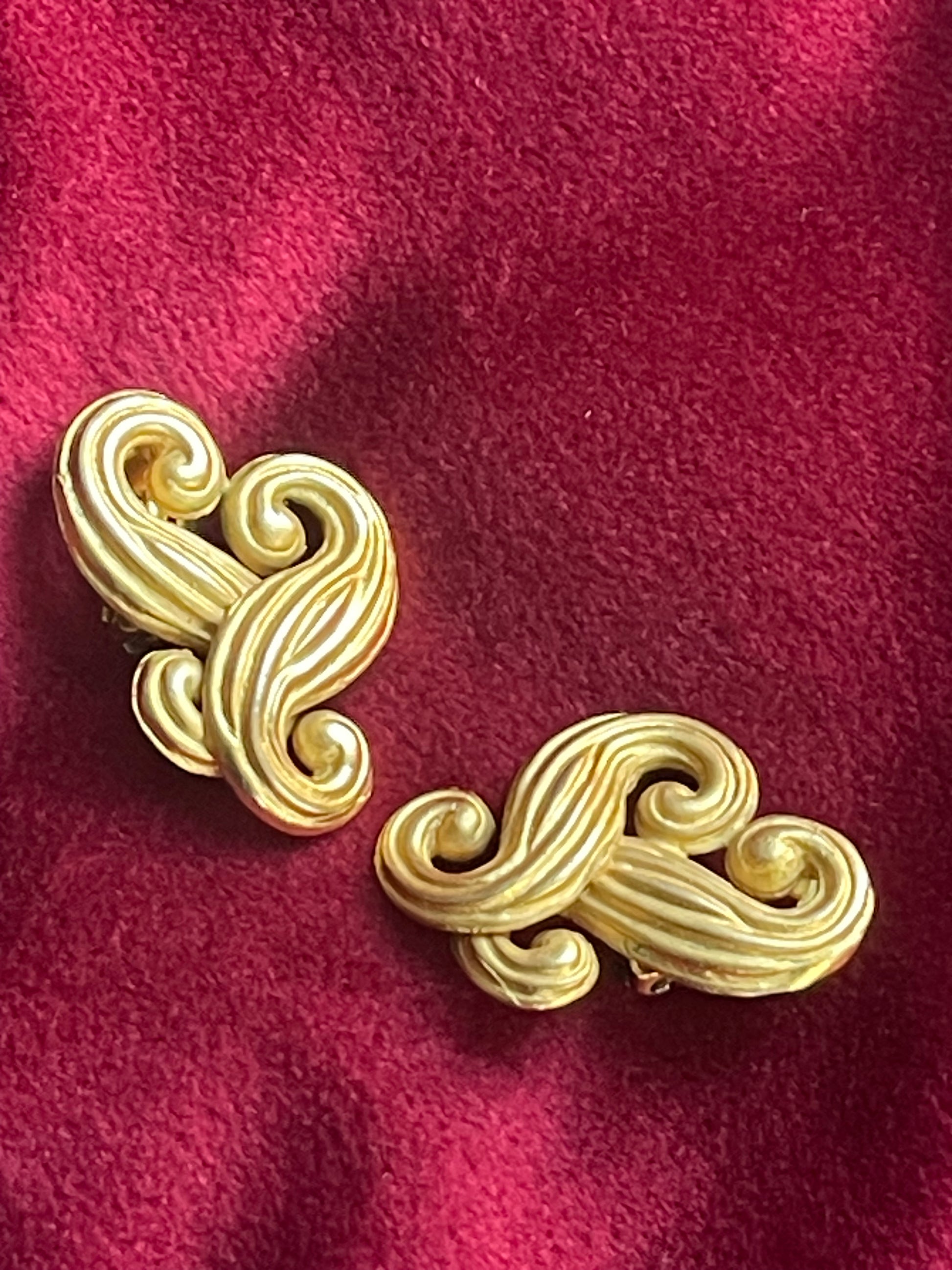 Vintage Nina Ricci swirly heart earrings in matte gold plated metal, signed Nina Ricci Paris, 1990s design on a red background 