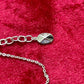 Close-up of the Dior necklace extension chain and oval logo tag on a red velvet background
