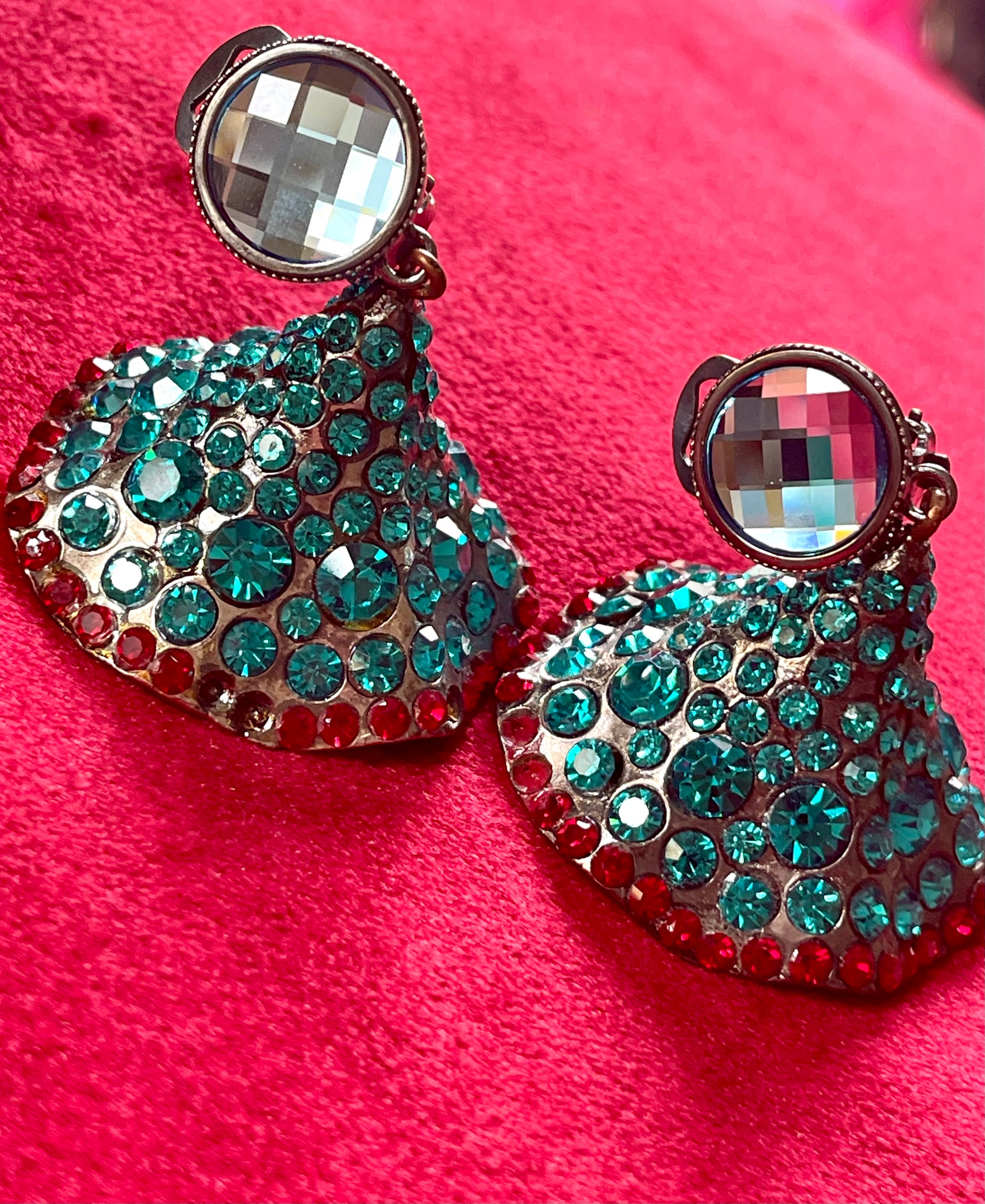 Close-up of Yves Saint Laurent Rive Gauche vintage statement earrings with turquoise and red rhinestones showing the imperfections with a red velvet background 