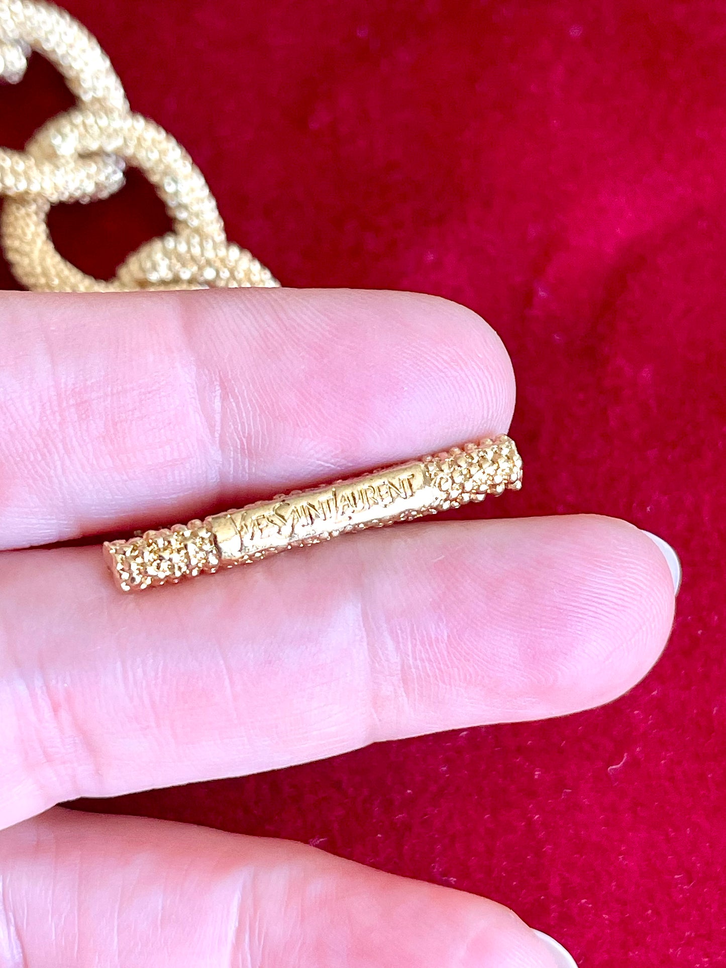 Signature detail view of YSL monogram charm hanging from gold vintage Yves Saint Laurent bracelet.