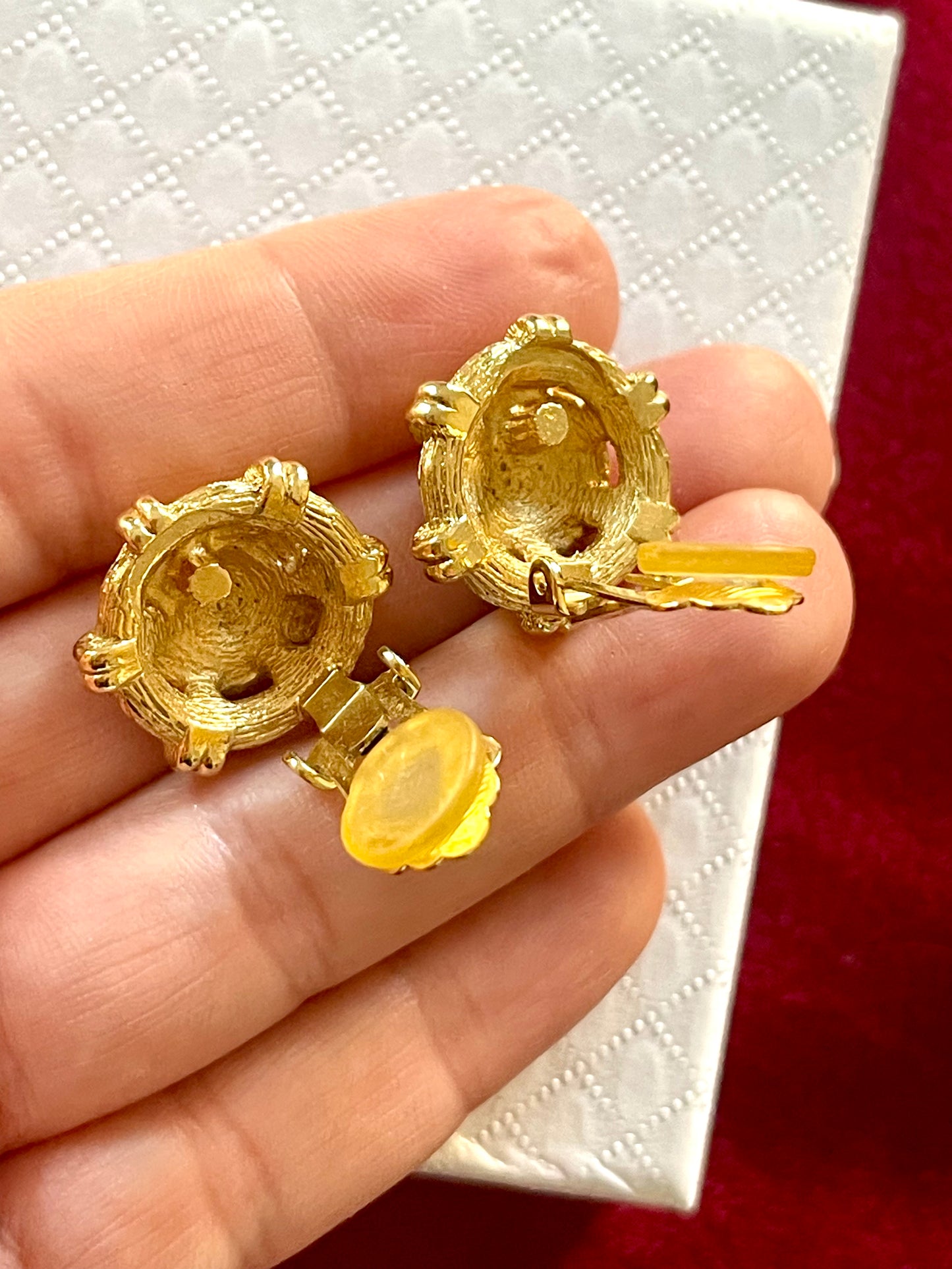 Backside view of vintage Christian Dior button earrings, held by hand against a pink background 