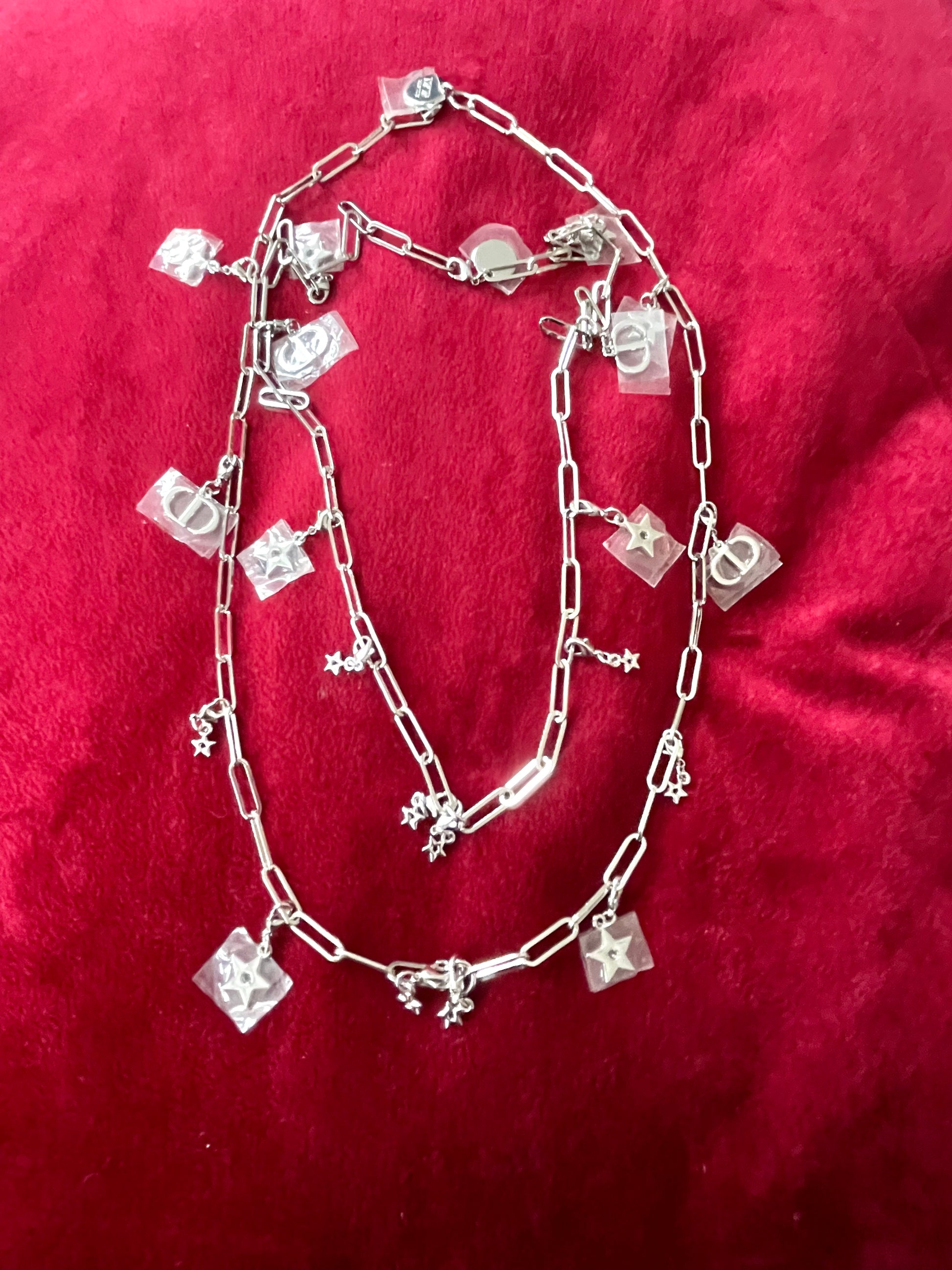 Two upcycled Dior Beauté phone charm necklace with removable silver-tone charms on a red background 