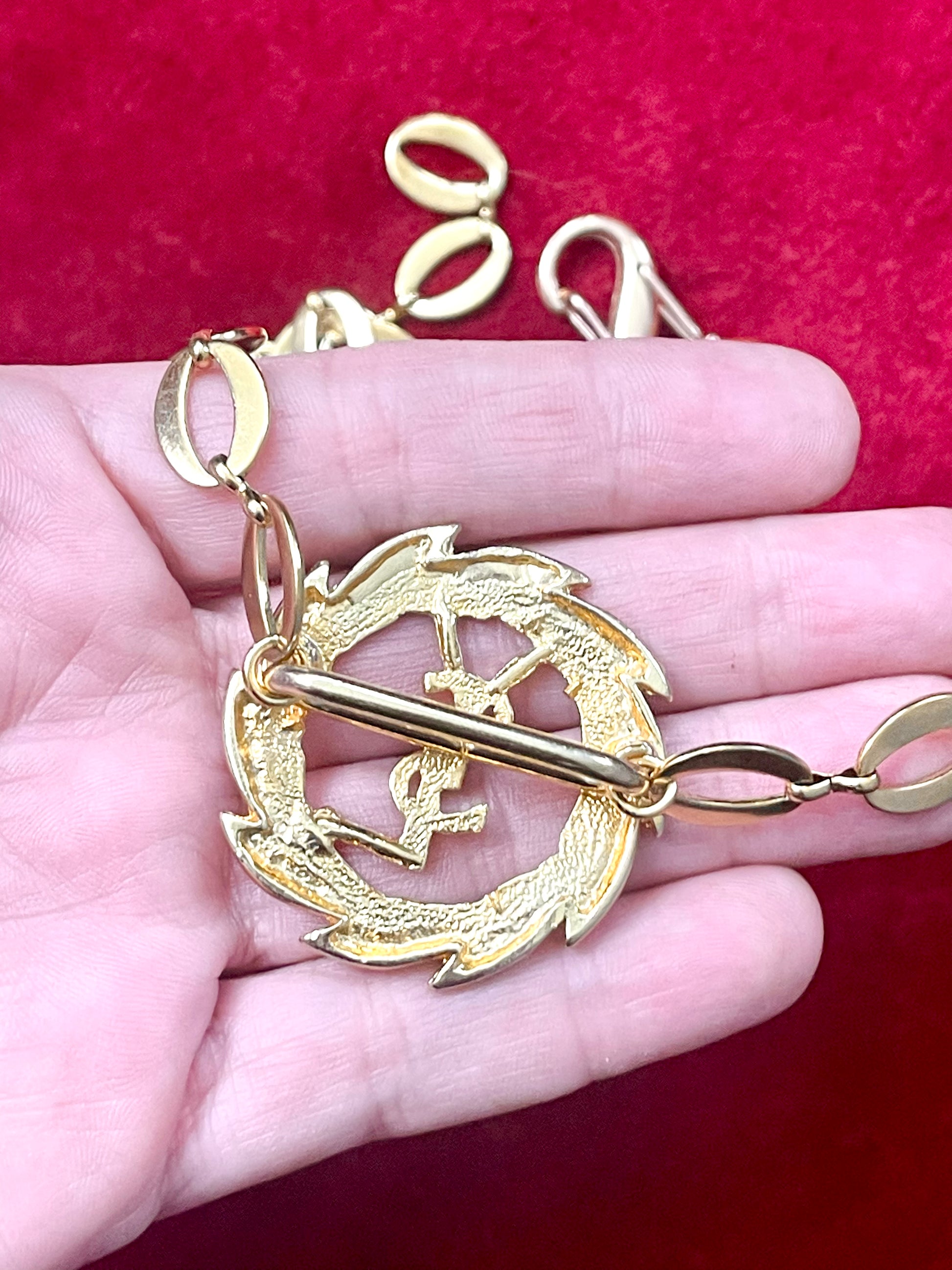 Held in hand , backside view of a refurbished vintage YSL laurel wreath pendant mounted on a gold-plated stainless steel necklace, with adjustable hoop links and a slightly lighter-toned closure.