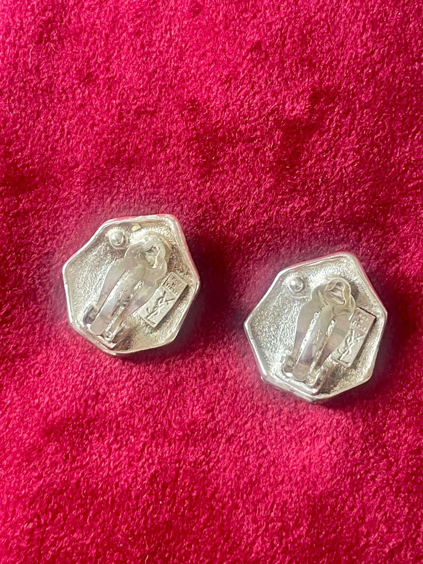 Back view of Pair of silver hexagonal Yves Saint Laurent vintage earrings on a red textured background
